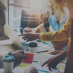 The DevOps Contact image shows a close up of people working around a table. On the table, you see papers, a laptop, coffee cups, water cups, etc.