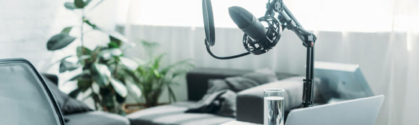 Test automation and software quality header. View of desk. On the desk is a laptop, notebook and pen, water glass. Next to the desk is a podcast mic.