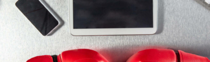 Overview of a table. A tablet, computer keyboard, and phone sit on the table. Also resting on the table is 2 red boxing gloves.