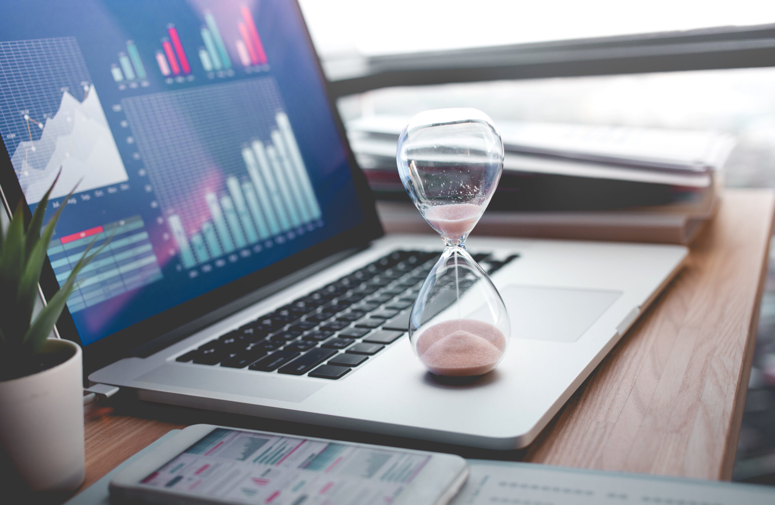 Business concepts with businessman holding hourglass with graph chart on computer laptop. Symbolizing the importance of time to market. 