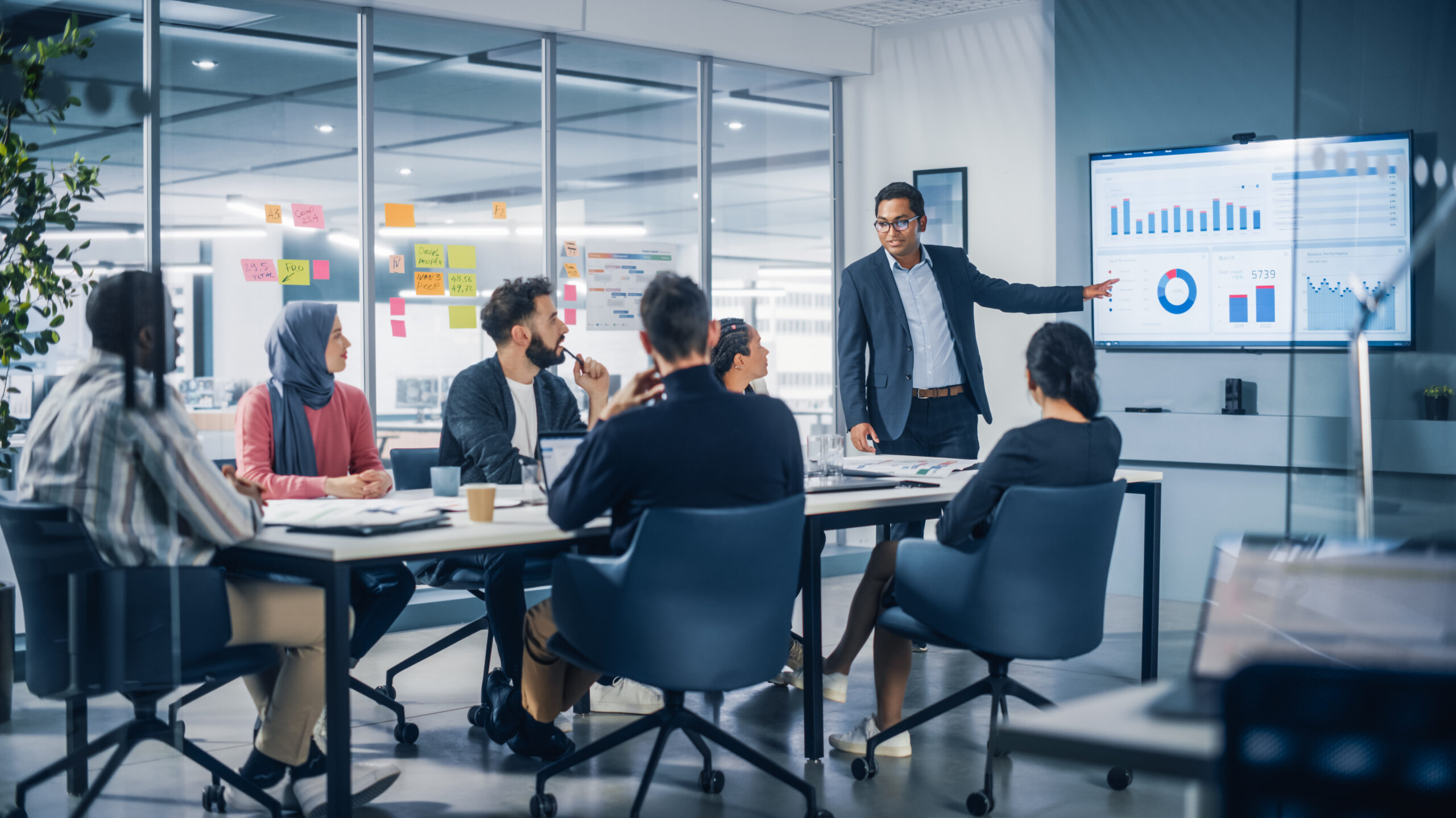 Presentation in Multi-Ethnic Office Conference Room. Meeting of Diverse Young Entrepreneurs, Specialists, Talking, Using TV for infographics. Businesspeople Develop e-Commerce Startup.